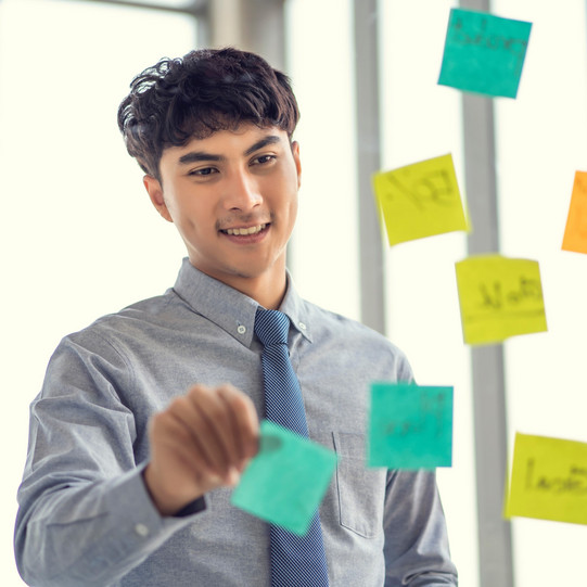 Young man in front of post-its stuck on glass wall. 