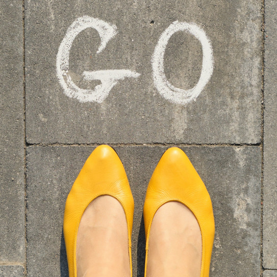 Photo: Women's feet in yellow ballerinas, on cobblestones, with the word "Go" written in chalk in front of them.