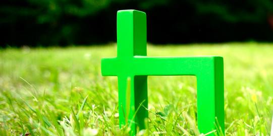 Ein grünes TU-Logo steht auf grünem Rasen. Daran lehnt ein Smartphone.